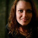A close-up portrait of a woman smiling warmly in dim lighting, enhancing her natural beauty.