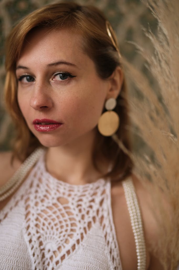 Alluring female with eyeliner in white knitted clothes looking at camera on blurred background