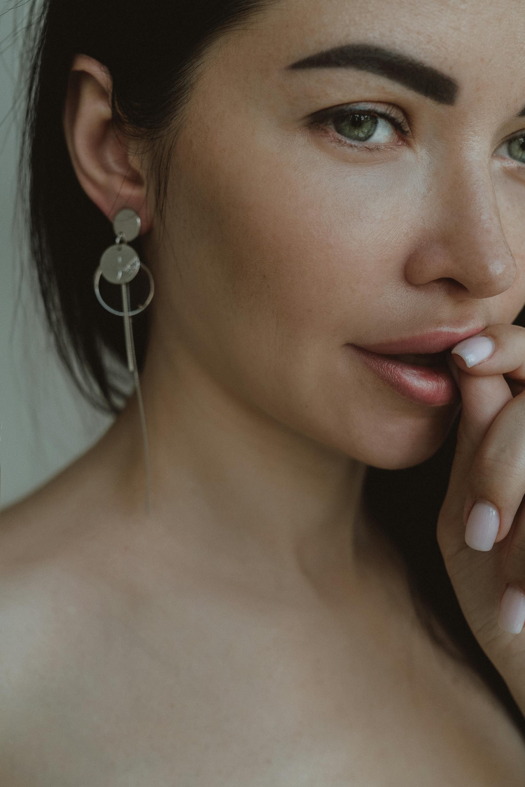 Close-up portrait of a woman wearing silver earrings and showing manicured nails.